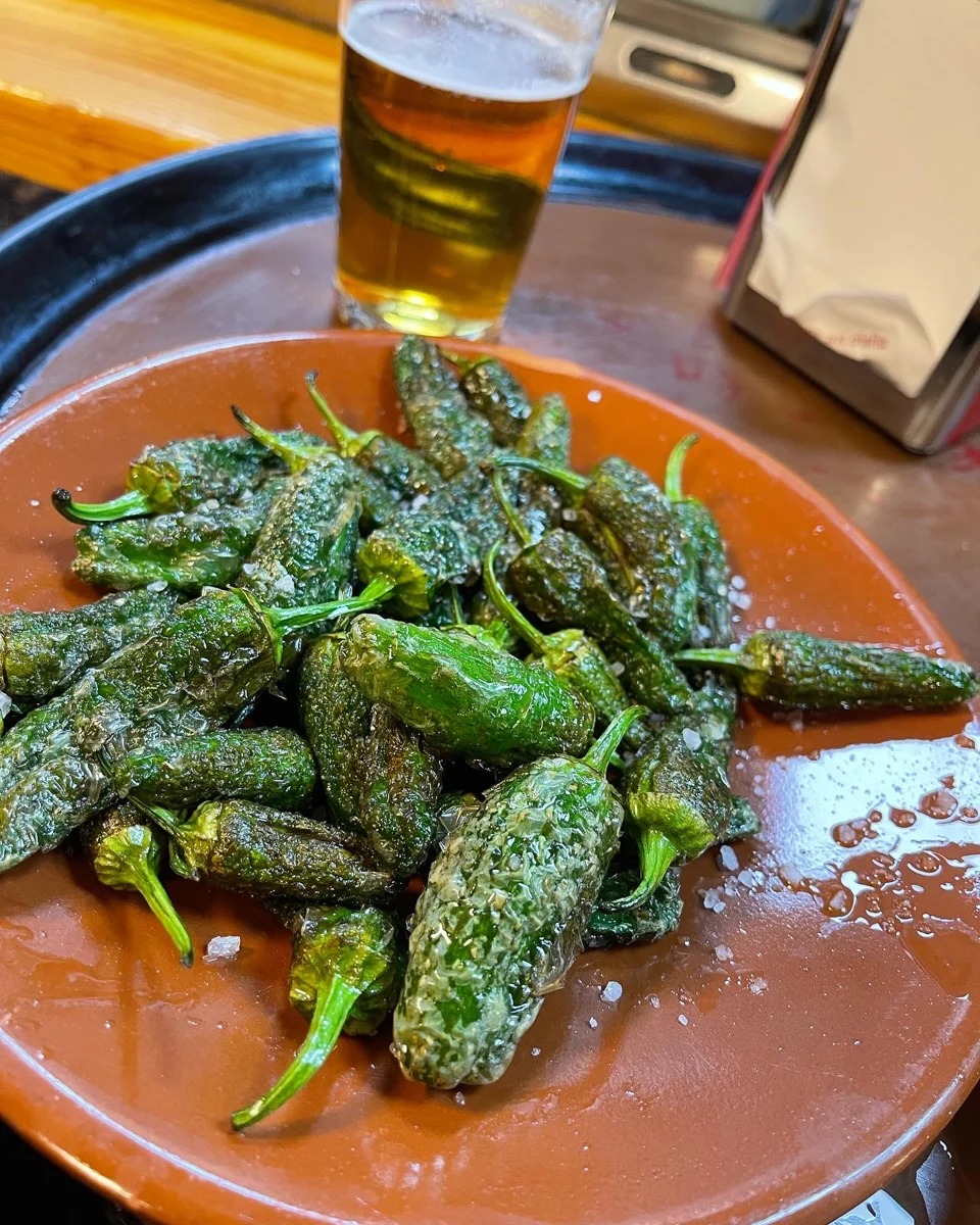 plate of pimientos de padron on a tray with a beer on the side of the tray.