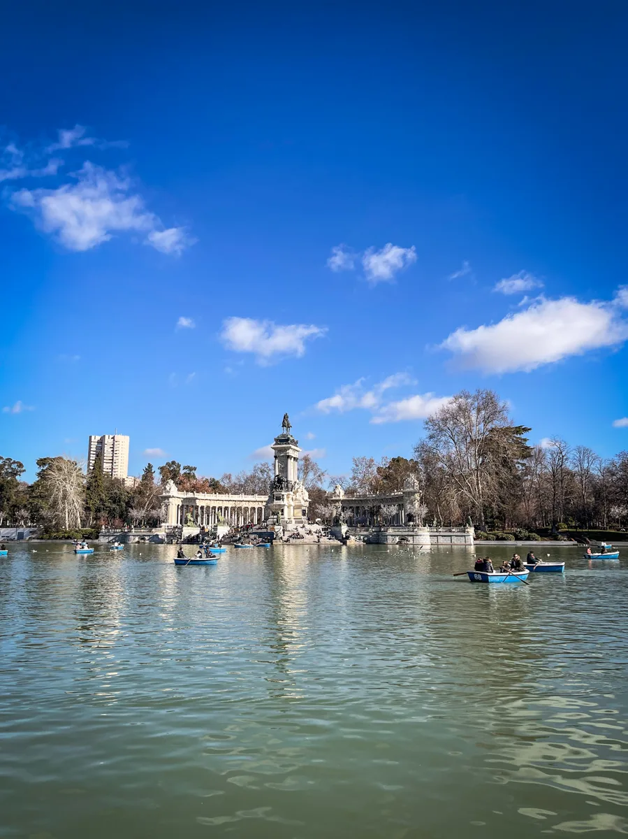 lake inside a park with a large stone monument at the back of the lake with bright blue skies and a few small white clouds.