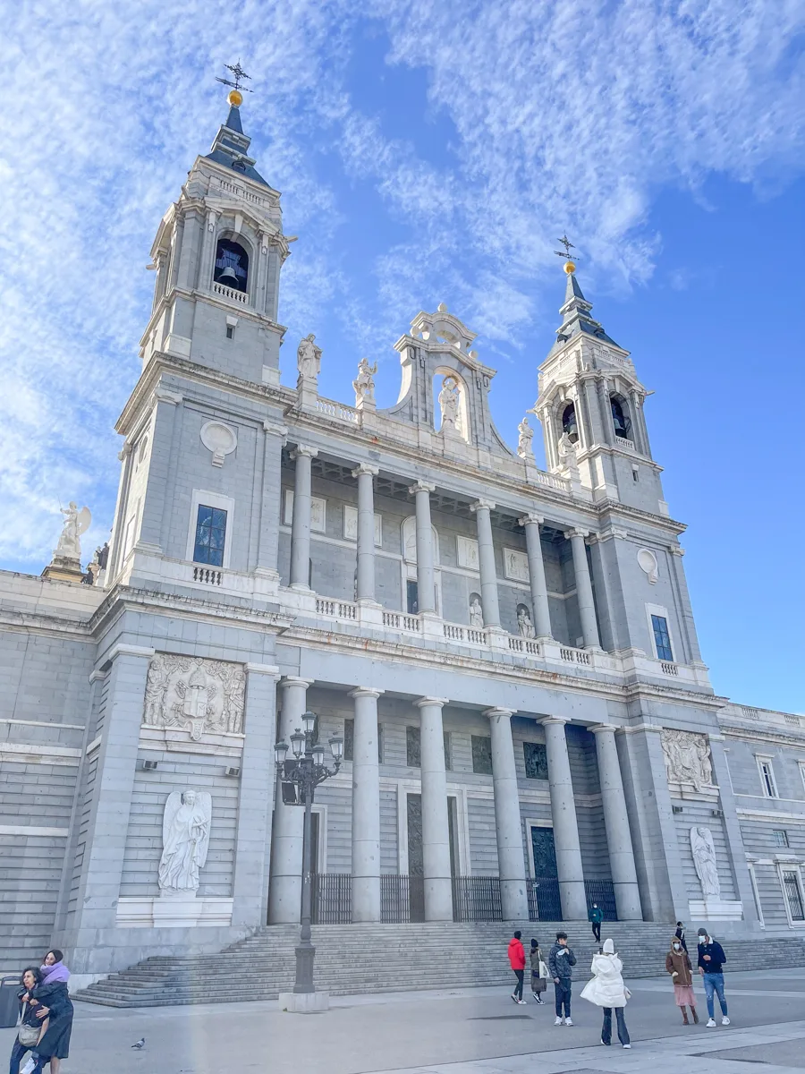 madrid cathedral with a light blue color on the outside and two large bell towers on either side of the structure and columns in the middle.